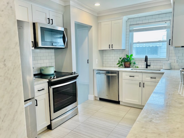 kitchen featuring ornamental molding, white cabinetry, a sink, appliances with stainless steel finishes, and backsplash