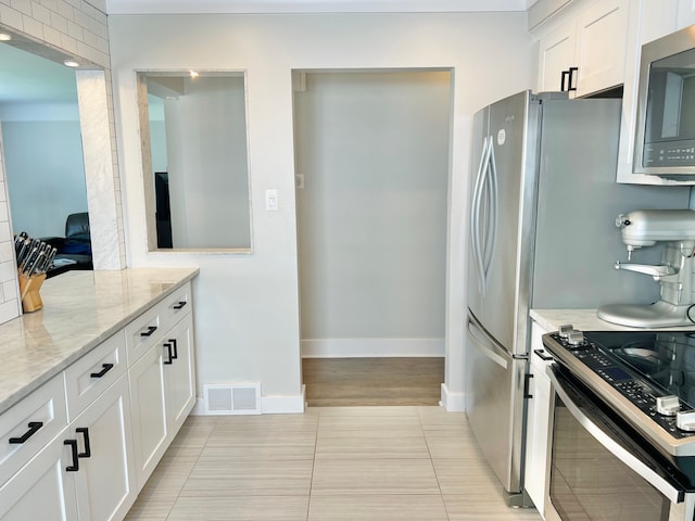 kitchen with visible vents, appliances with stainless steel finishes, light tile patterned floors, light stone counters, and white cabinetry