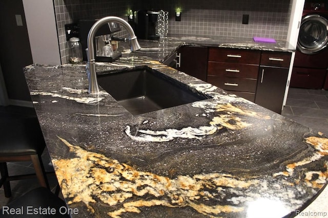 details featuring a sink, dark stone counters, dark brown cabinetry, and tasteful backsplash
