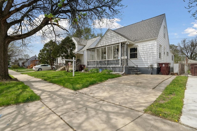 view of front of house featuring a sunroom, a front lawn, roof with shingles, and concrete driveway
