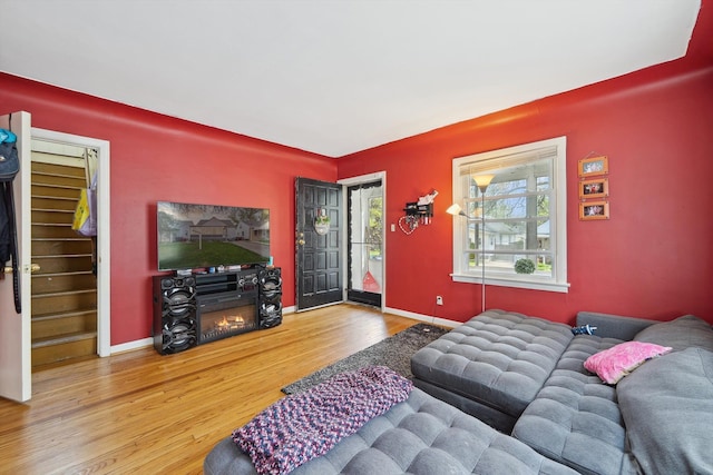 living room featuring baseboards, a lit fireplace, and wood finished floors
