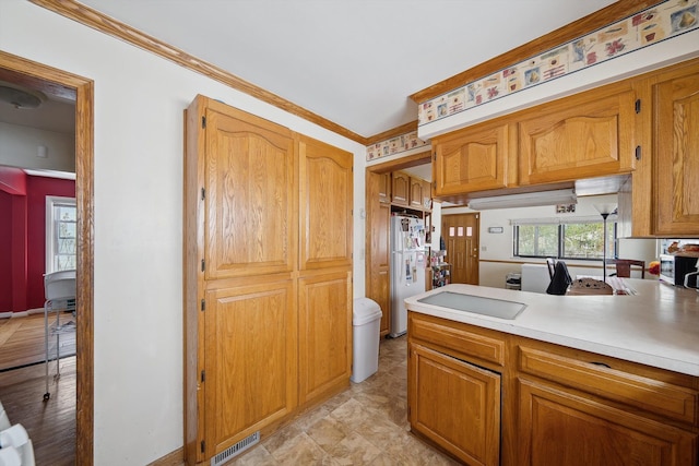 kitchen with visible vents, brown cabinets, light countertops, freestanding refrigerator, and ornamental molding
