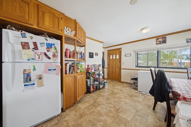 kitchen featuring crown molding, stone finish floor, freestanding refrigerator, and brown cabinetry