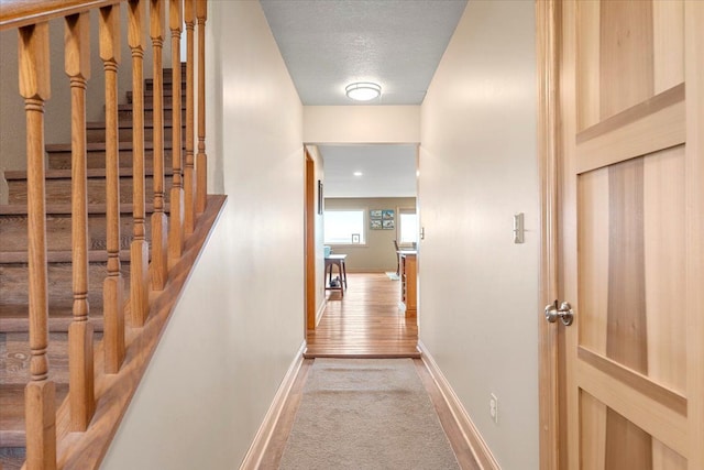corridor featuring baseboards, light carpet, and stairway