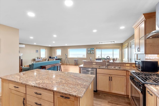 kitchen with light brown cabinetry, wall chimney range hood, appliances with stainless steel finishes, a sink, and light wood-style flooring