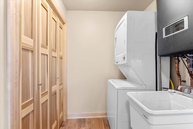 clothes washing area featuring laundry area, baseboards, stacked washing maching and dryer, a sink, and light wood finished floors