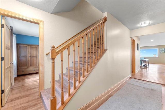 staircase featuring a textured ceiling, baseboards, and wood finished floors