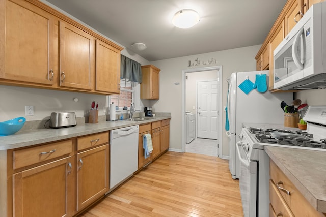 kitchen featuring a sink, white appliances, light countertops, light wood-style flooring, and washer / clothes dryer