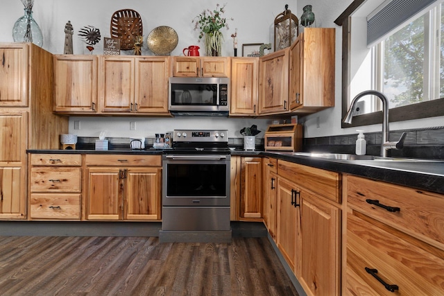 kitchen with brown cabinetry, dark countertops, a sink, stainless steel appliances, and dark wood-type flooring