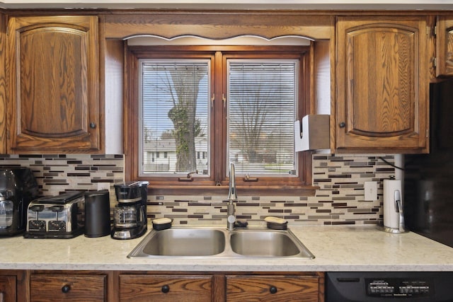 kitchen with brown cabinetry, tasteful backsplash, dishwasher, a sink, and light countertops