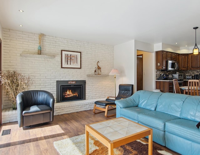 living area featuring a brick fireplace, recessed lighting, wood finished floors, and visible vents