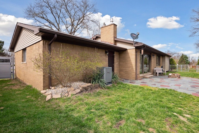 back of house featuring a chimney, a lawn, brick siding, fence, and a patio