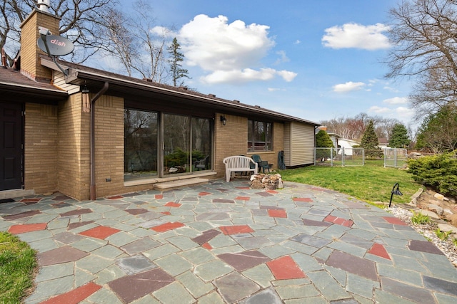 rear view of property with a chimney, a lawn, brick siding, fence, and a patio
