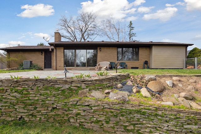 rear view of house featuring fence, a patio, a chimney, and brick siding