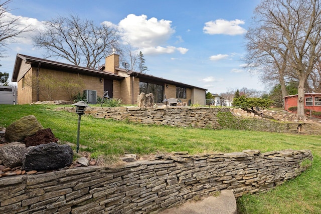 back of property featuring a yard, brick siding, a chimney, and central air condition unit
