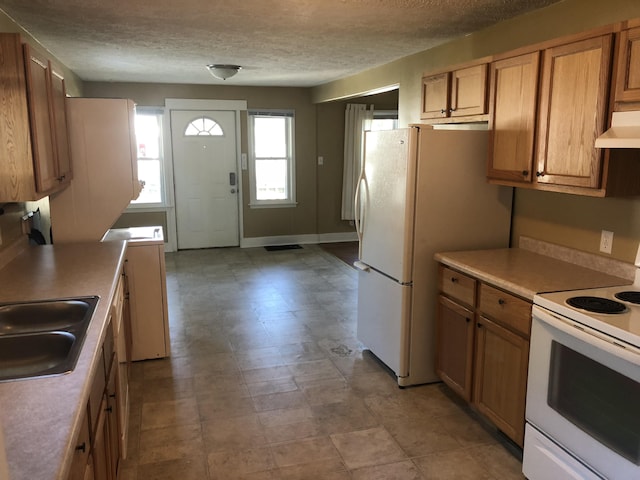 kitchen with brown cabinetry, white appliances, a textured ceiling, under cabinet range hood, and a sink
