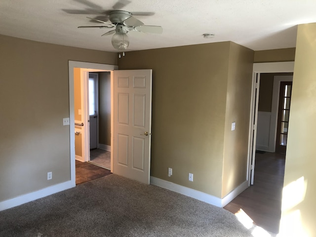 spare room featuring dark colored carpet, baseboards, and ceiling fan