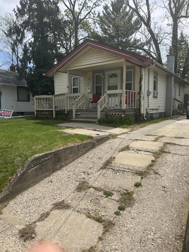 view of front of home with covered porch, a chimney, and a front lawn