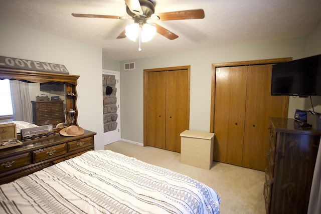 bedroom featuring two closets, a ceiling fan, visible vents, and light carpet