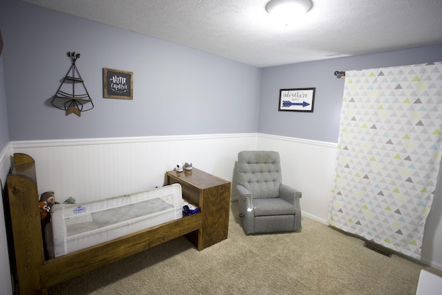 bedroom with carpet, wainscoting, a textured ceiling, and visible vents