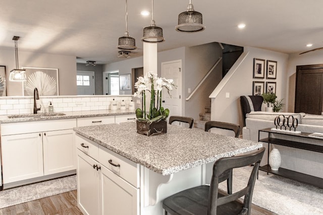 kitchen featuring hanging light fixtures, a sink, light wood finished floors, white cabinetry, and a kitchen bar
