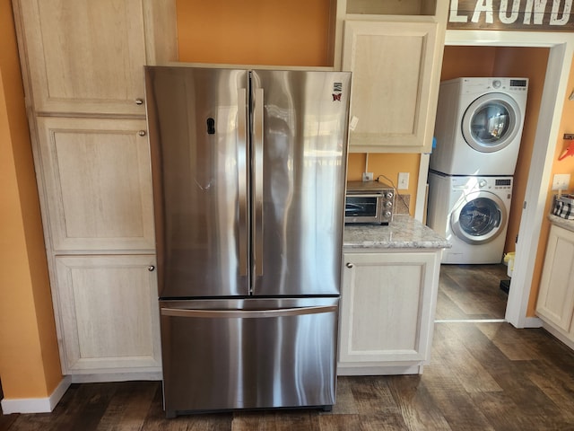 kitchen featuring freestanding refrigerator, light brown cabinetry, a toaster, stacked washing maching and dryer, and dark wood-type flooring