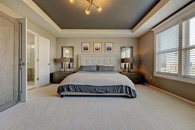 carpeted bedroom with baseboards, multiple windows, a raised ceiling, and ensuite bath