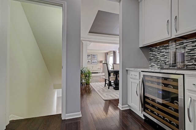 bar featuring beverage cooler, baseboards, tasteful backsplash, indoor bar, and dark wood-style floors