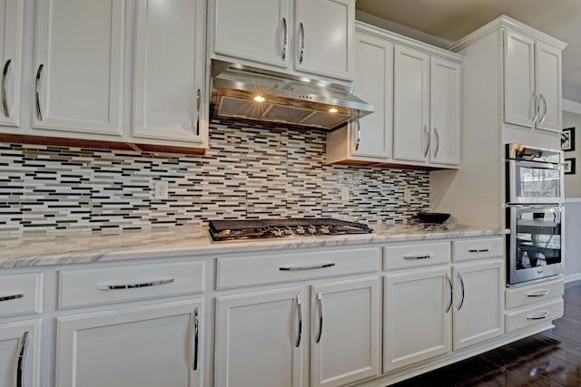 kitchen featuring appliances with stainless steel finishes, white cabinets, under cabinet range hood, and tasteful backsplash
