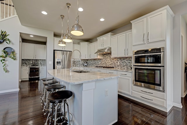 kitchen featuring appliances with stainless steel finishes, a sink, dark wood finished floors, wine cooler, and under cabinet range hood