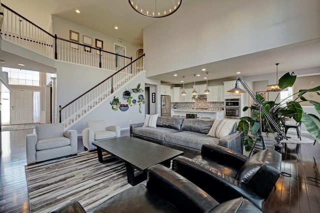 living area with an inviting chandelier, dark wood-style flooring, a towering ceiling, stairway, and recessed lighting