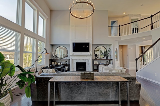 living room with an inviting chandelier, dark wood-style flooring, a high ceiling, stairway, and a premium fireplace