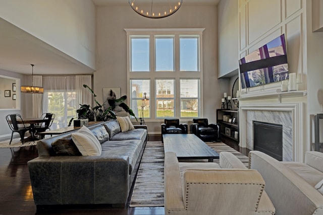living area with a fireplace, baseboards, a high ceiling, hardwood / wood-style flooring, and a notable chandelier