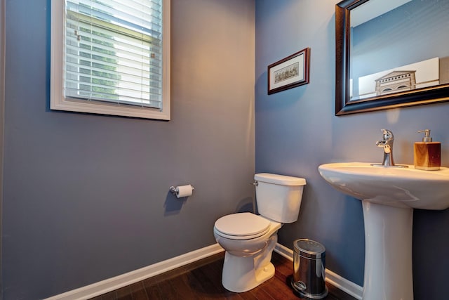 half bath with toilet, baseboards, a sink, and wood finished floors