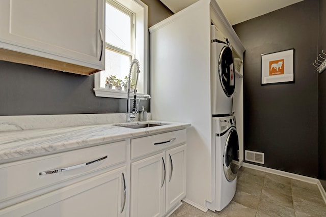 washroom featuring visible vents, stacked washer and dryer, baseboards, a sink, and cabinet space