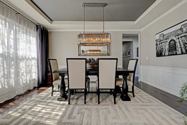 dining space featuring crown molding, a raised ceiling, wood finished floors, and a notable chandelier