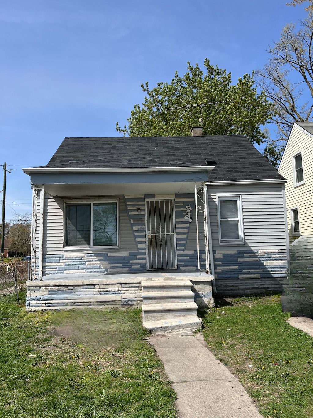 bungalow with roof with shingles, covered porch, a chimney, and a front yard