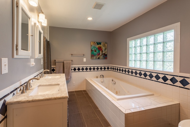 full bathroom with visible vents, tile walls, wainscoting, a sink, and a whirlpool tub