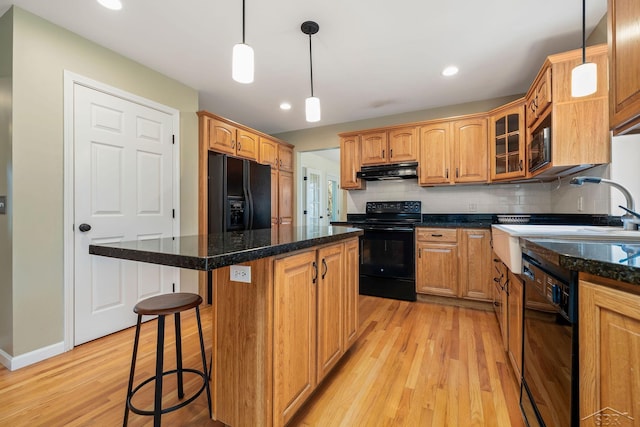 kitchen featuring a kitchen island, under cabinet range hood, black appliances, and light wood-type flooring