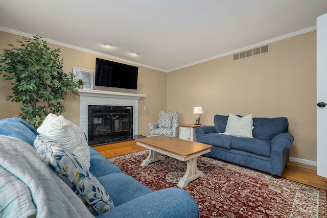 living area featuring crown molding, visible vents, a glass covered fireplace, and wood finished floors