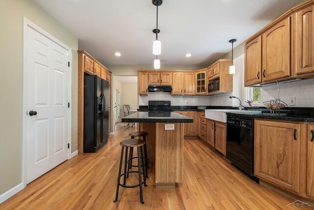 kitchen featuring light wood-style flooring, a breakfast bar area, under cabinet range hood, and black appliances