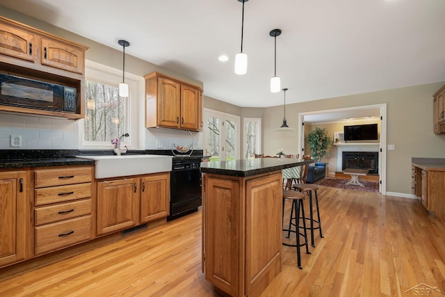 kitchen featuring a sink, a kitchen breakfast bar, black appliances, and light wood-style flooring