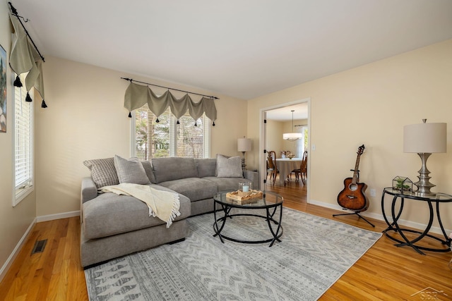 living room featuring baseboards, a chandelier, wood finished floors, and visible vents