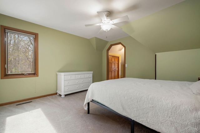 carpeted bedroom featuring ceiling fan, arched walkways, baseboards, vaulted ceiling, and visible vents