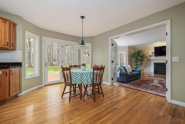 dining space with baseboards, a fireplace with raised hearth, and light wood-type flooring