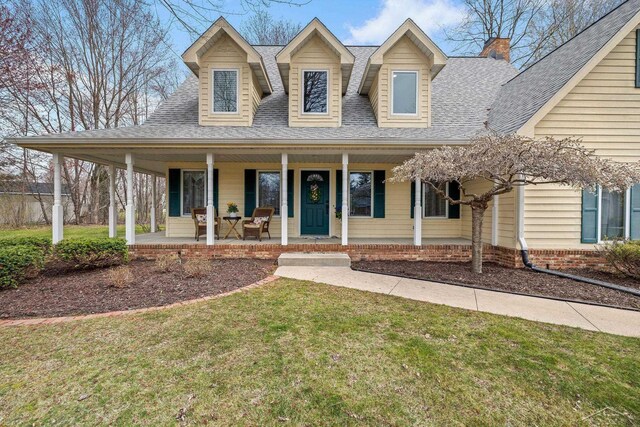 farmhouse-style home with a porch, a chimney, roof with shingles, and a front lawn