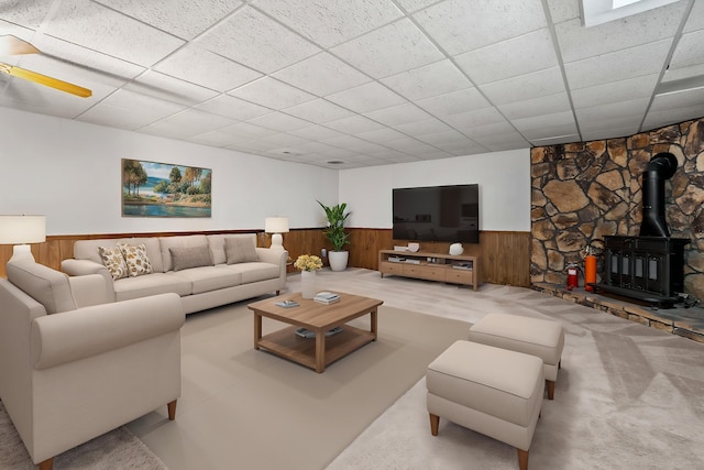 living room with wooden walls, a wainscoted wall, a wood stove, and a paneled ceiling