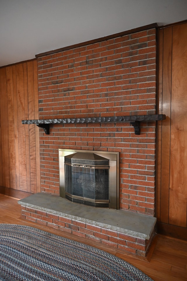 details featuring a brick fireplace, wood walls, and wood finished floors