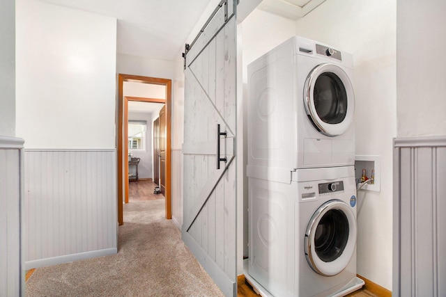 washroom with laundry area, light colored carpet, a barn door, baseboards, and stacked washer / dryer