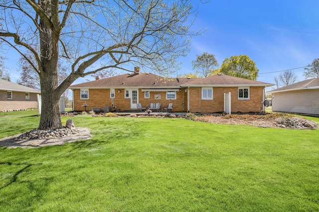 back of property with a lawn, brick siding, a chimney, and a patio